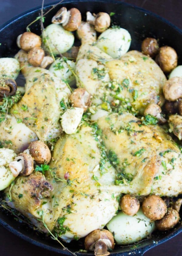 a whole butterflied chicken smothered with herb butter in a black skillet with mushrooms, onions and garlic ready to be cooked