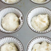 a silver muffin pan lined with paper molds half-filled with muffins batter.