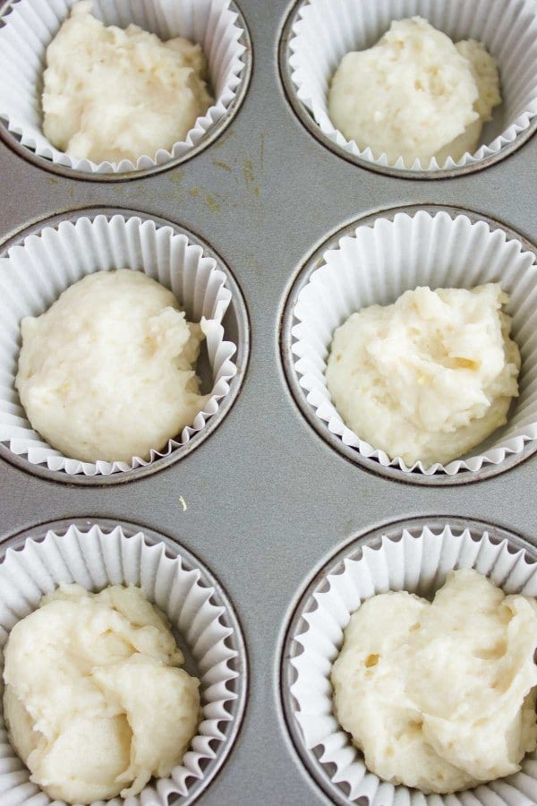 a silver muffin pan lined with paper molds half-filled with muffins batter.