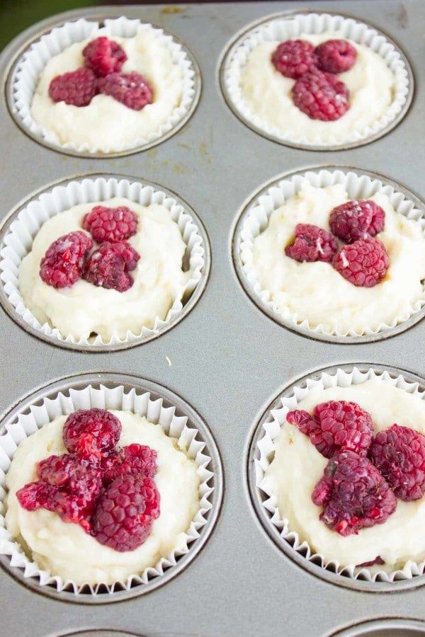 a paper-mold lined muffin tray filled with unbaked muffin batter topped with fresh raspberries.