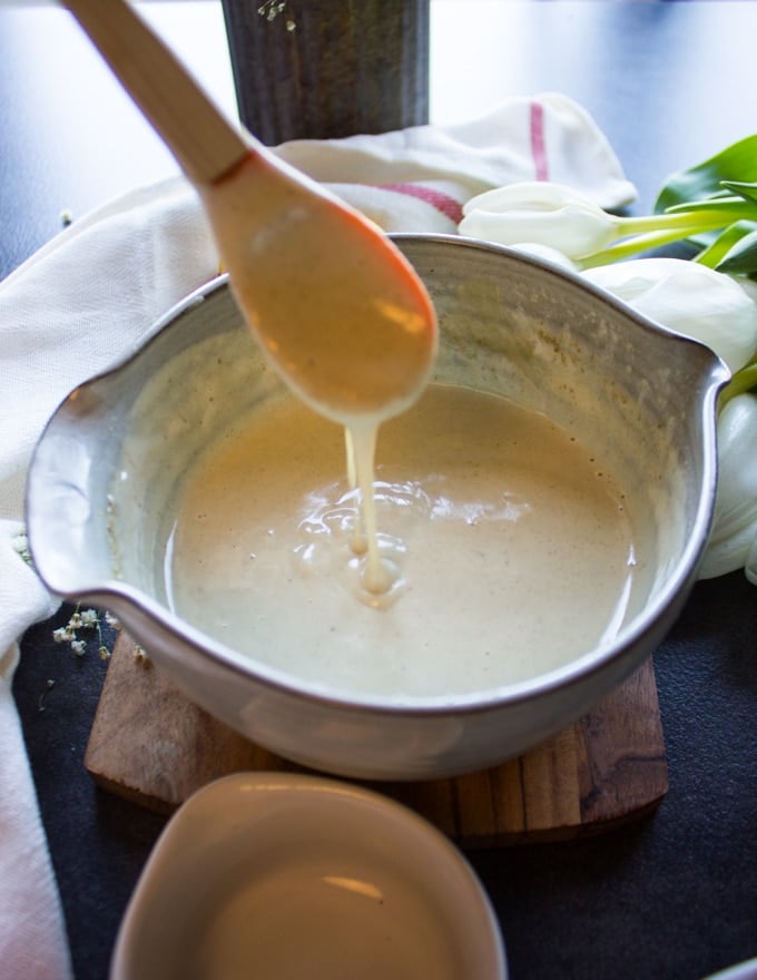 The tahini sauce is all mixed up and ready in a bowl and a spoon trying to scoop it out to show the creamy texture 