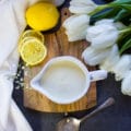 The tahini sauce in a pouring cu with lemon slices around it and white flowers, and a tea towel