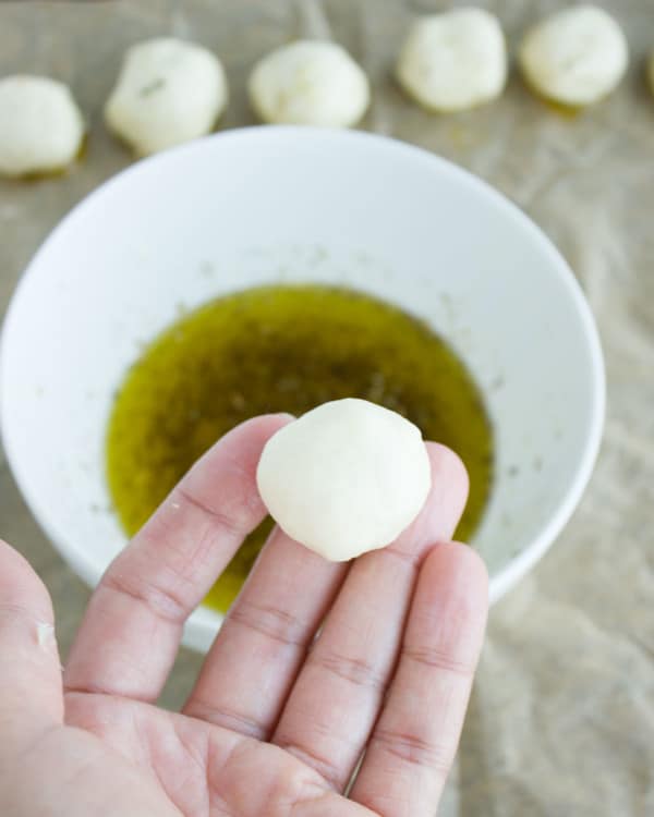 a little ball of pizza dough held above a small dish with seasoned olive oil