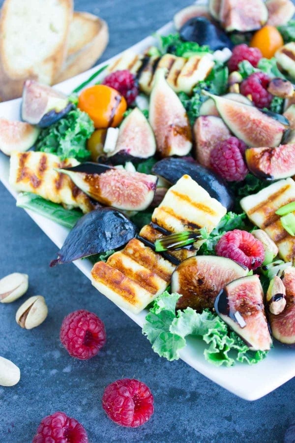 Grilled Halloumi Salad drizzled with balsamic reduction and topped with fresh figs and raspberries on a big white plate placed on a blue rustic table.