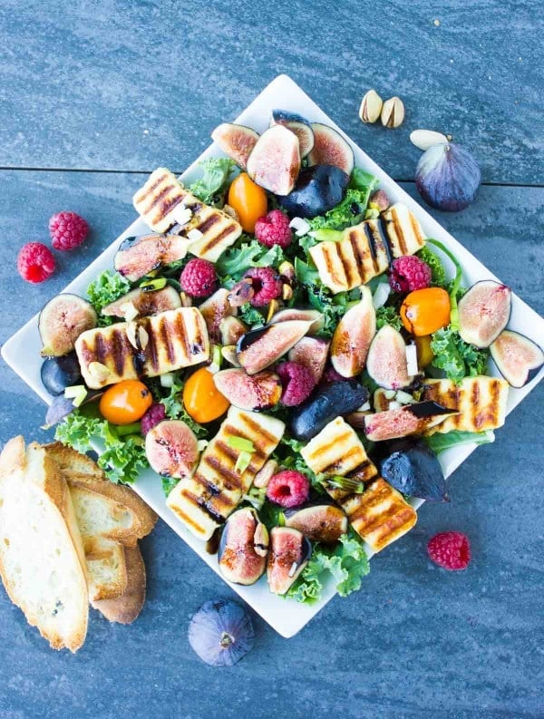 Grilled Halloumi Salad drizzled with balsamic reduction and topped with fresh figs and raspberries on a big white plate placed on a blue rustic table.