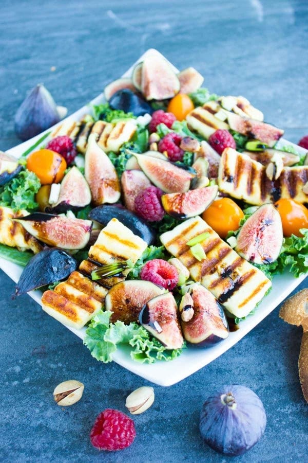 Grilled Halloumi Salad drizzled with balsamic reduction and topped with fresh figs and raspberries on a big white plate placed on a blue rustic table.