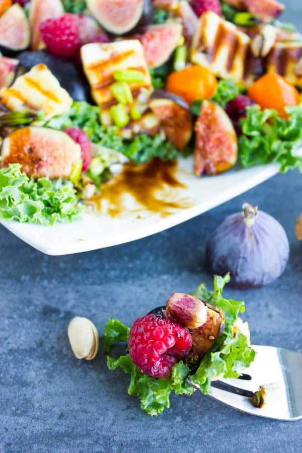 a fork full of Grilled Halloumi Salad in front of a plate with more salad topped with fresh fruit and nuts.