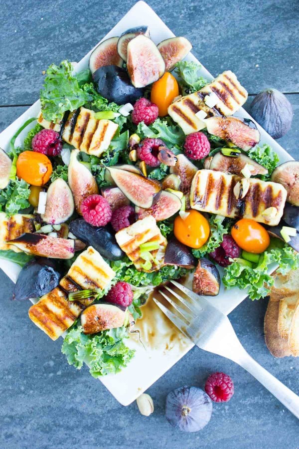 Grilled Halloumi Salad drizzled with balsamic reduction and topped with fresh figs and raspberries on a big white plate placed on a blue rustic table.