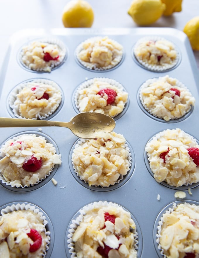 A spoon adding the crunch tropping over the raspberry muffins recipe right before baking