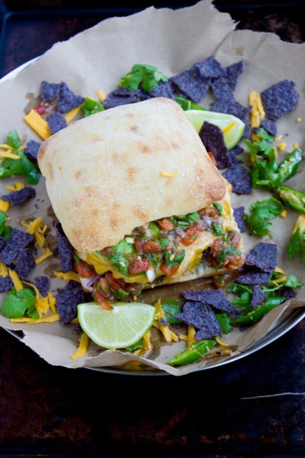 top view of the juicy burger loaded with fajita toppings served on a tray with tortilla chips and lime wedges 