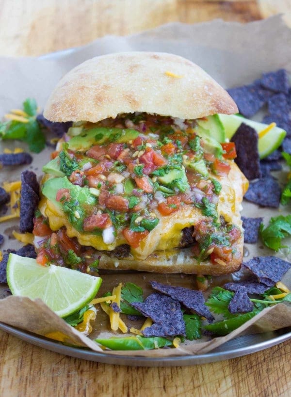 A variety of fajita toppings over the juicy burgers including salsa, guacamole, cilantro, jalapeños, avocados and tortilla chips