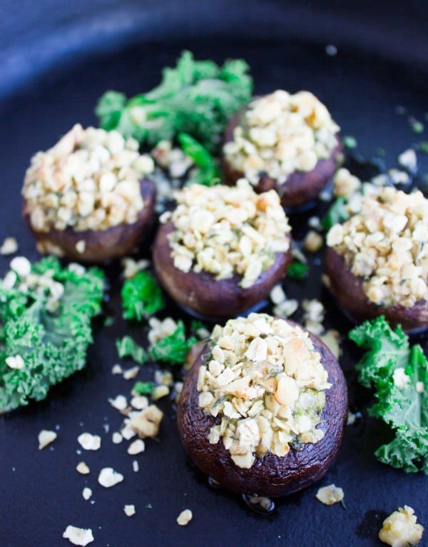 Kale Pesto Stuffed Mushrooms with crunchy walnut topping lined up on a black plate with some kale leaves as decoration