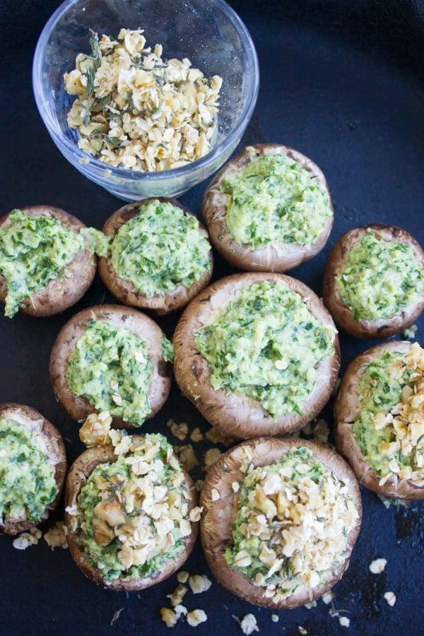raw cremini mushrooms stuffed with kale pesto ready to be topped with walnut crust and be baked 