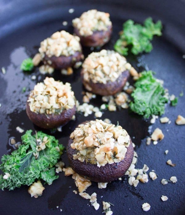 Easy Stuffed Mushrooms with crunchy walnut topping lined up on a black plate with some kale leaves as decoration