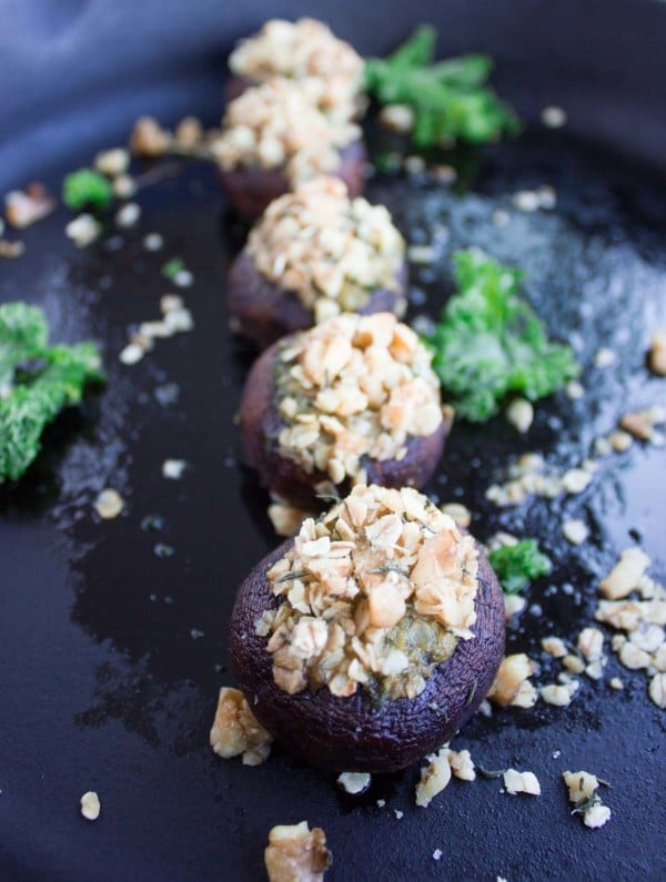 Kale Pesto Stuffed Mushrooms with crunchy walnut topping lined up on a black plate with some kale leaves as decoration