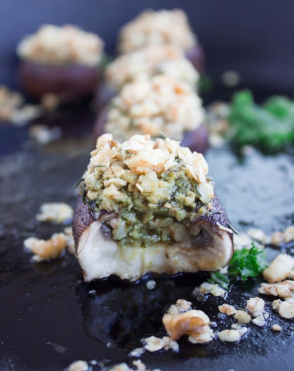 Easy Stuffed Mushrooms with kale pesto and crunchy walnut topping lined up on a black plate