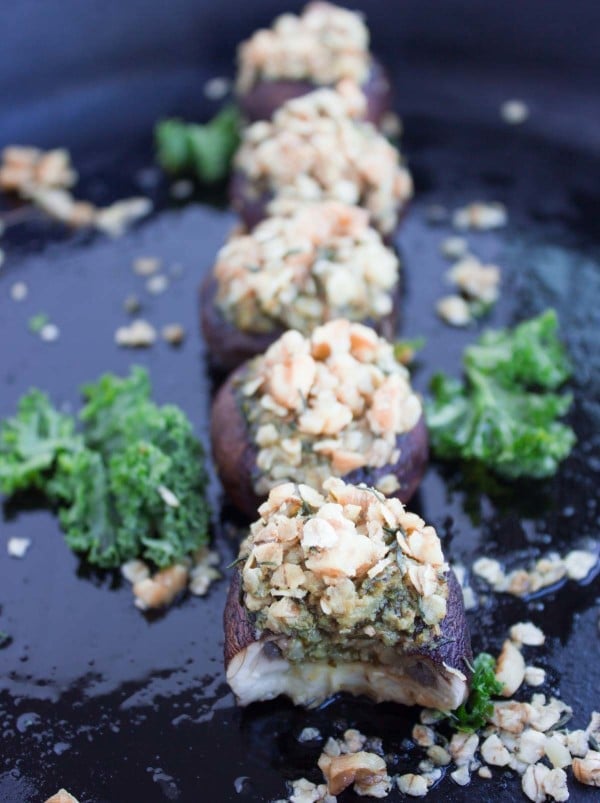 Kale Pesto Stuffed Mushrooms with crunchy walnut topping lined up on a black plate with some kale leaves as decoration