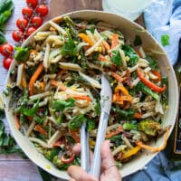 Tossing the pasta primavera together in a bowl with tongs.
