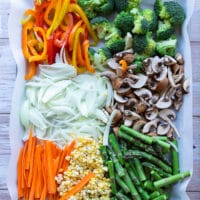 Spring veggies on a sheet pan lined with parchment: yellow peppers, broccoli, onions, mushrooms, carrots, corn, and asparagus.