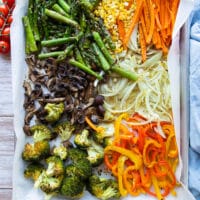 Roasted Spring veggies on a sheet pan lined with parchment: yellow peppers, broccoli, onions, mushrooms, carrots, corn, and asparagus.