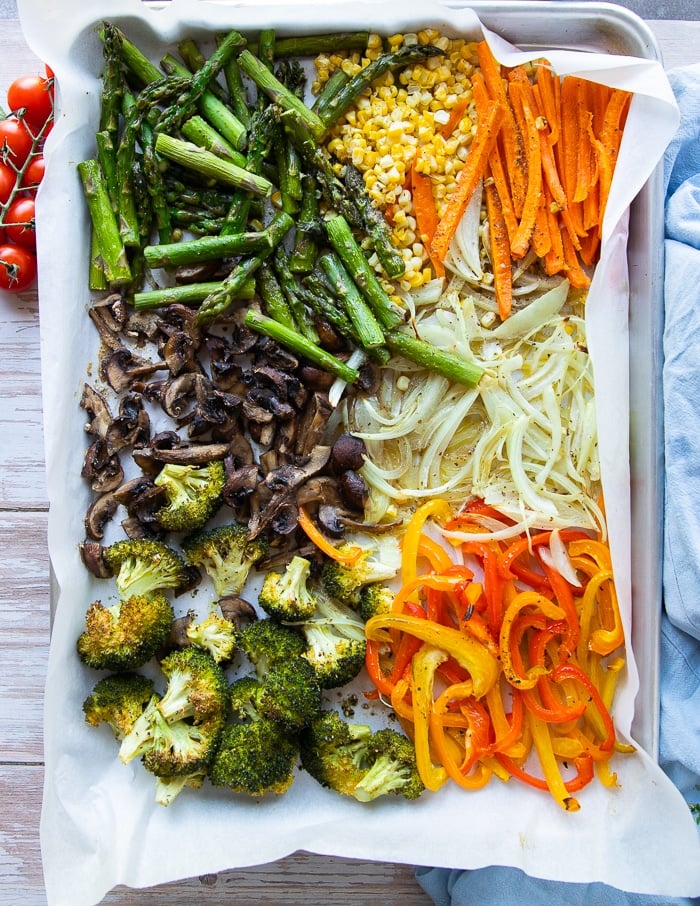 Roasted Spring veggies on a sheet pan lined with parchment: yellow peppers, broccoli, onions, mushrooms, carrots, corn, and asparagus.