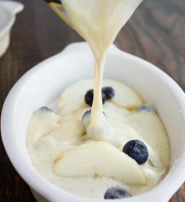 vanilla bean custard being poured on top of pears and blueberries to make clafoutis