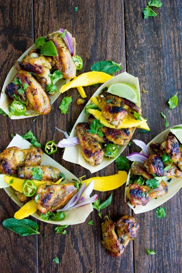 Overhead shot of Sweet and Spicy Chicken Wings smothered in Mango Chutney and served in small paper dishes with some fresh cilantro and mango slices