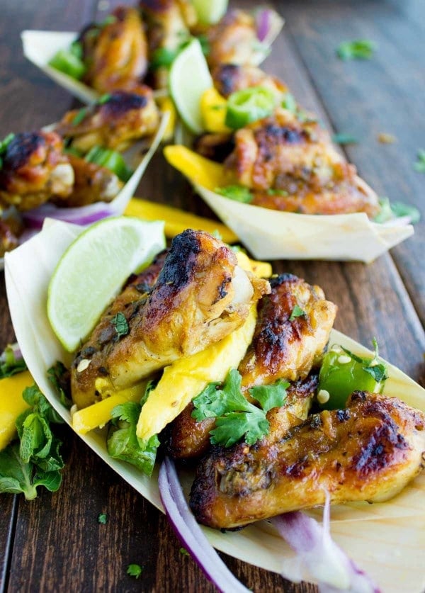 close-up of a serving of sweet and spicy chicken wings smothered in mango chutney, served in a small oval paper boat