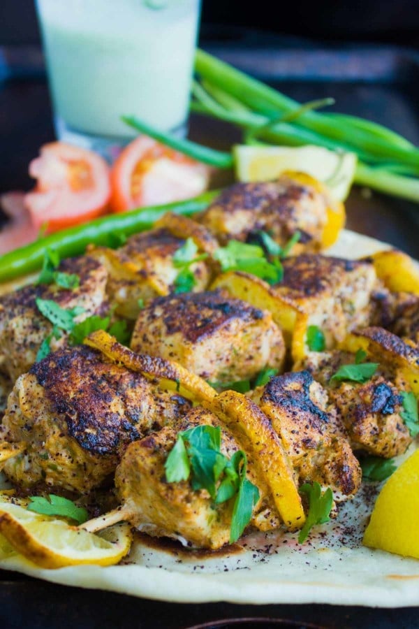 Turkish Style Grilled Chicken Skewers served on a white plate with a glass of Ayran and some veggies in the background