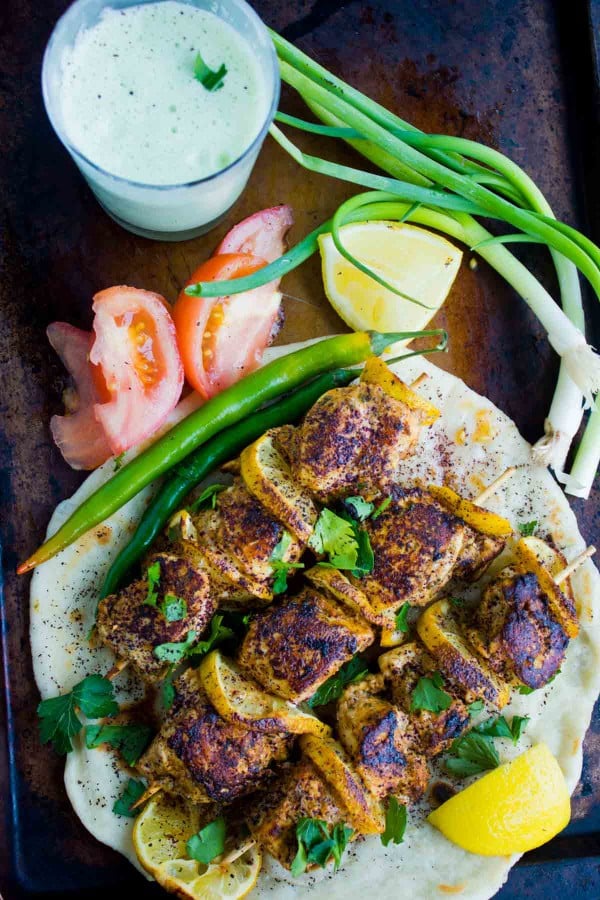 Turkish Style Chicken Skewers served on a big pita, with some veggies and a glass of Ayran in the background