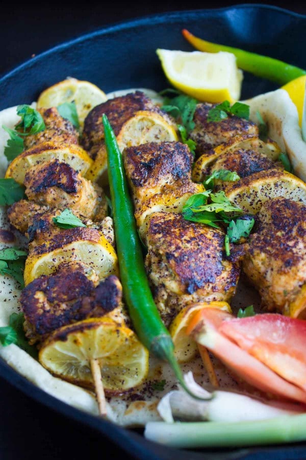 sumac- sprinkled Turkish Style Grilled Chicken Skewers placed in a black skillet with some chilies and lemon wedges