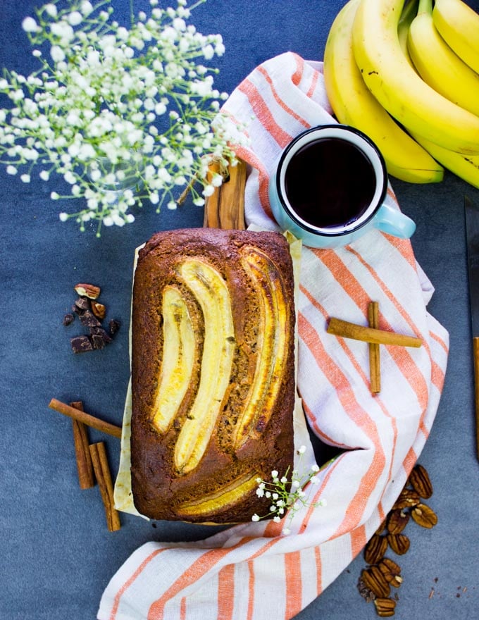 Whole Wheat Banana Bread Loaf topped with bananas and surrounded by a tea towel and a cup of coffeee