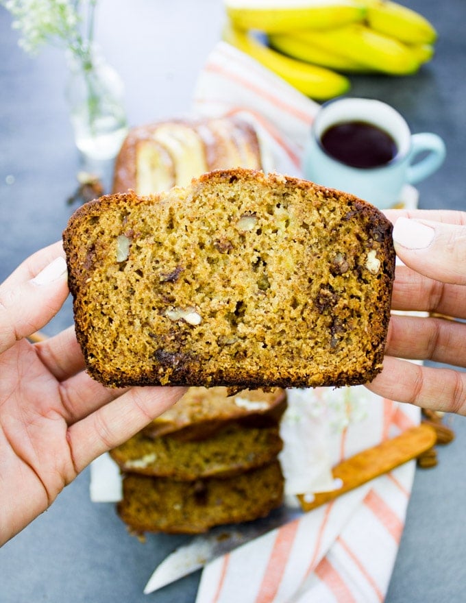 A hand holding a slice of whole wheat banana bread close up showing the airy texture, chocolate chunks and pecans