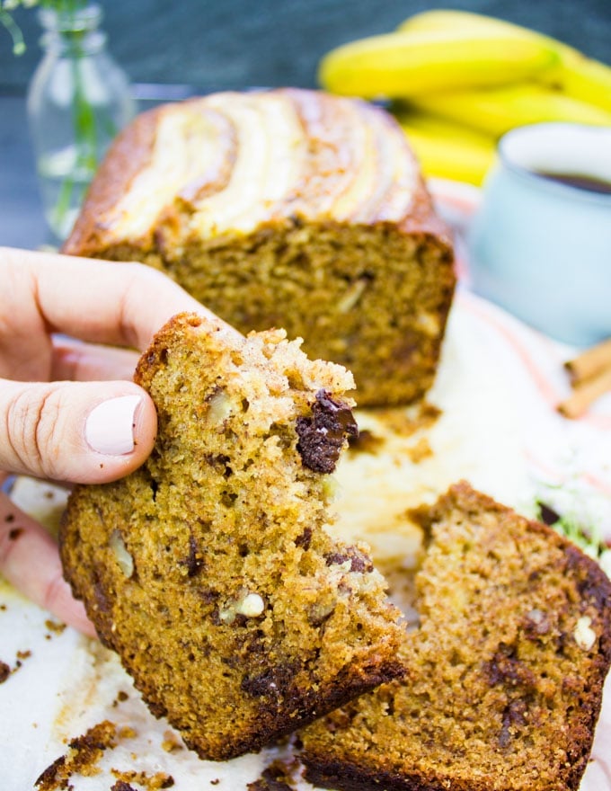 A hand holding a bitten slice of whole wheat banana bread