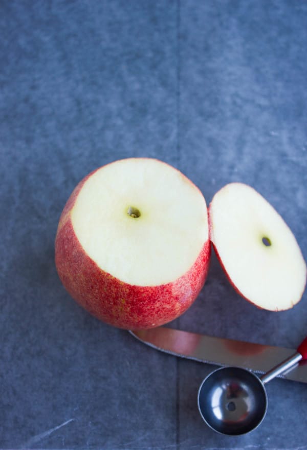 a red apple with the top cut of with a knife and melon baller next to it