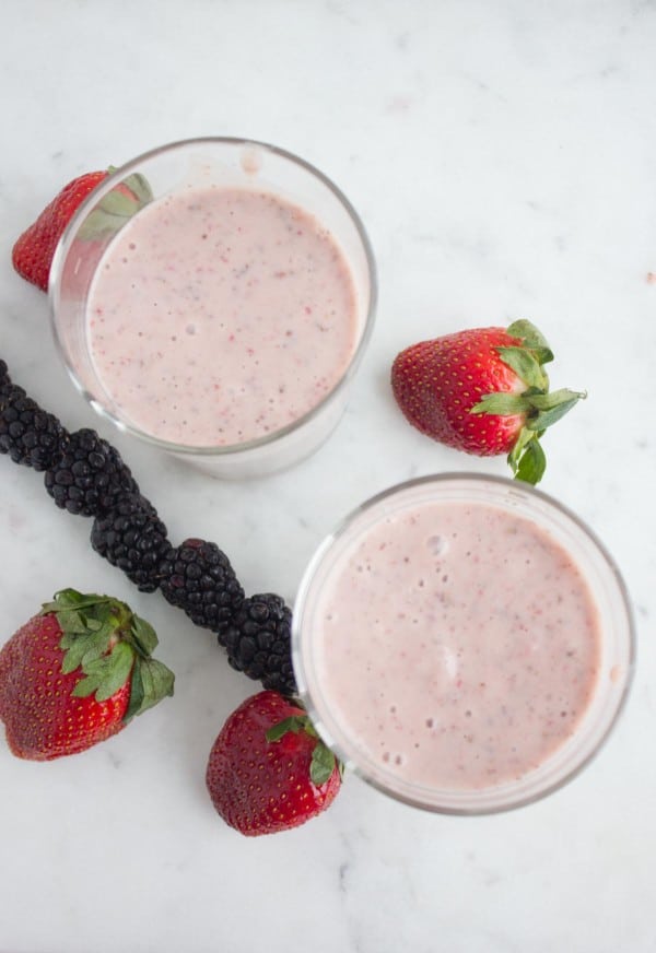 Overhead shot of 2 glasses of Banana Berry Avocado Chia Smoothie on a white kitchen counter with a blackberry skewer and some fresh strawberries