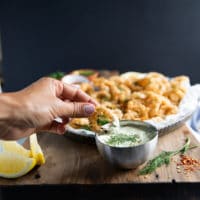 A hand dipping the fried calamari in tartar sauce