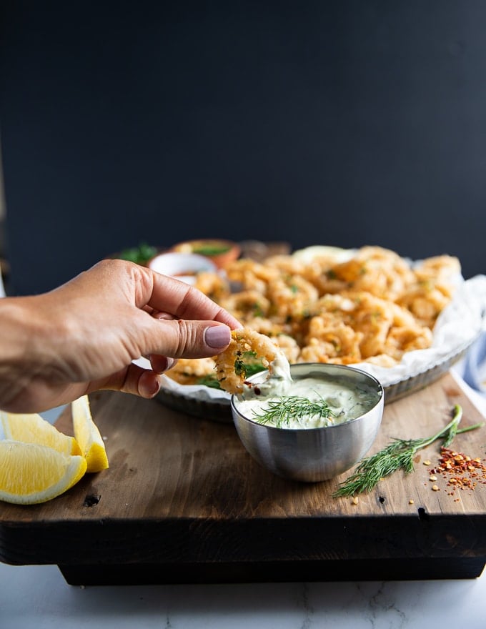 A hand dipping the fried calamari in tartar sauce