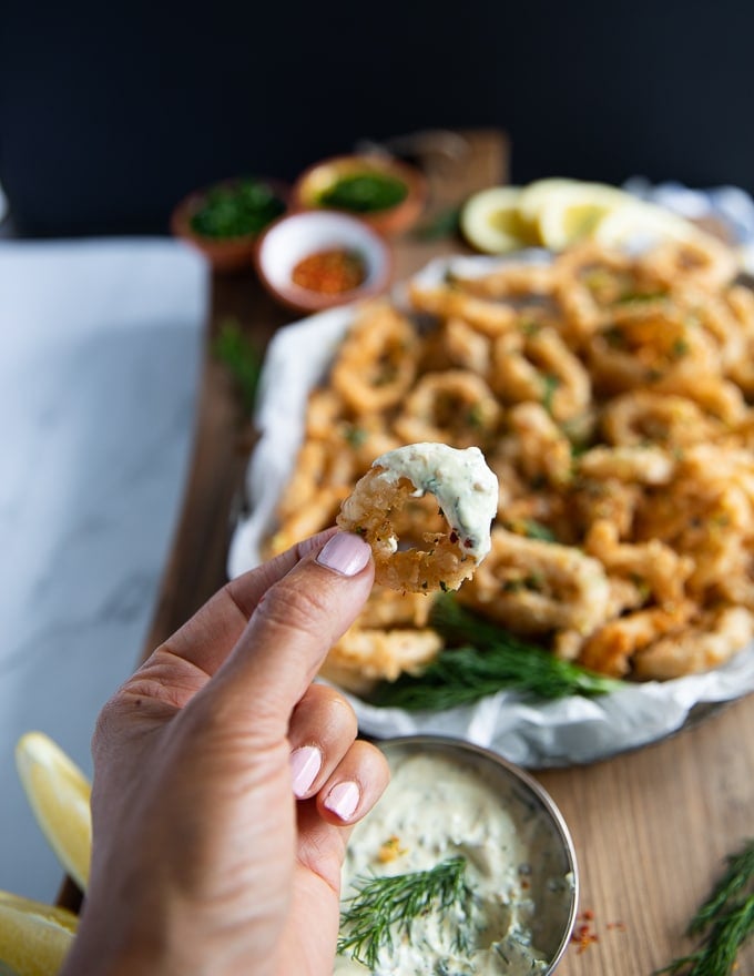 A hand holding a calamari dipped already in tartar sauce showing the sauce and calamari