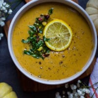 A close up bowl of one Mediterranean Soup or Autumn Squash soup topped with lemon slices, pistou and surrounded by pumpkin