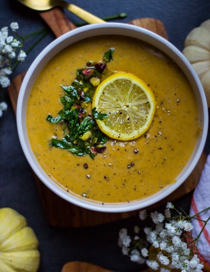 A close up bowl of one Mediterranean Soup or Autumn Squash soup topped with lemon slices, pistou and surrounded by pumpkin