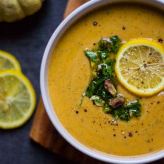 A half a bowl of Mediterranean soup or autumn squash soup toped with lemon slice and crunchy pistachio and parsley