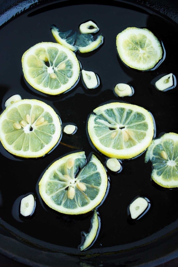 lemon slices and sliced garlic placed in a black skillet with a small amount of olive oil.