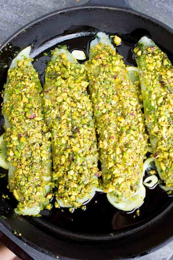 Four Pesto Pistachio Fish Fillets neatly lined up in a black skillet ready for the oven.