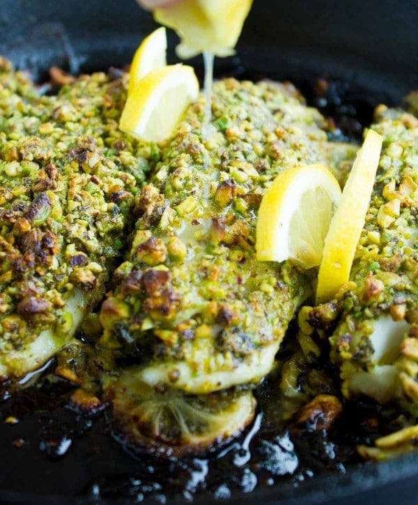 a lemon being squeezed on Pesto Pistachio Fish Fillets with crunchy golden brown pistachio crusts served in a black skillet.