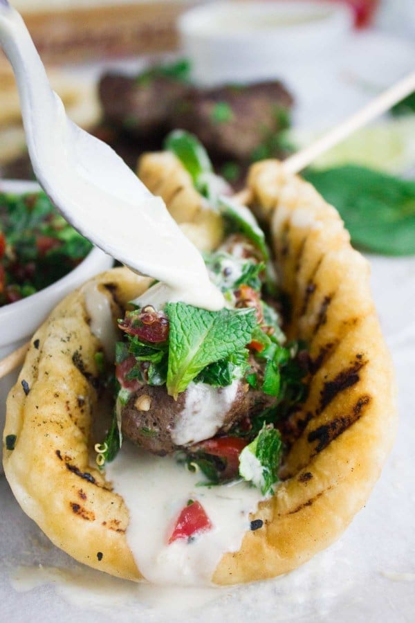 lamb kebab wrap and a spoon drizzling some tahini sauce over the lamb wrap