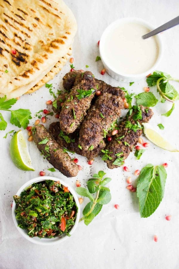 Top view of lamb kebabs grilled, some tahini sauce on the side, tabouleh salad and fresh mint