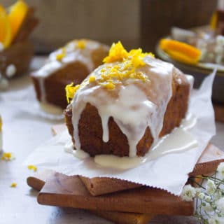 Close up of one orange carrot cake glazed and topped with orange zest over a wooden coaster.