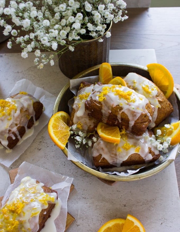 A plate of orange carrot cakes glazed and piled surrounded by orange slices