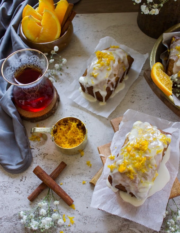 two orange carrot cakes surrounded by a cup of tea and cinnamon sticks